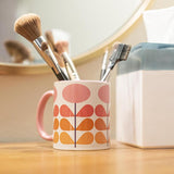 1959s mid century modern pink flowers on a white background coffee mug. Has ombre orange to yellow leaves. Inside of mug is pink, and the handle is also pink. This photo shows the mug filled with paint brushes
