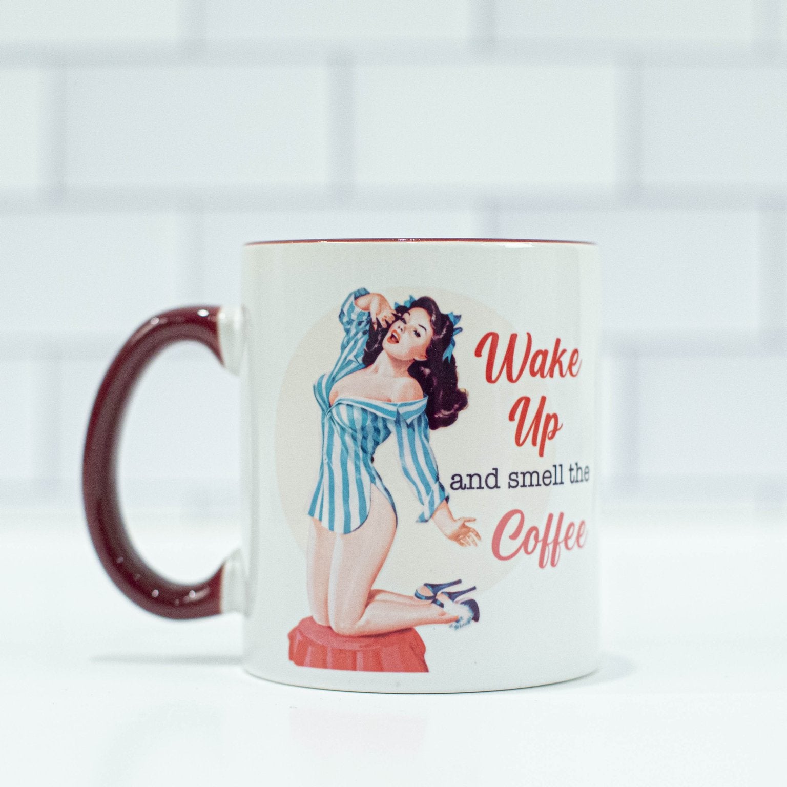 1950s style brunette pinup with a blue and white striped nightshirt on next to the words "wake up and smell the coffee" on a cream colored background. Mug has a maroon colored handle