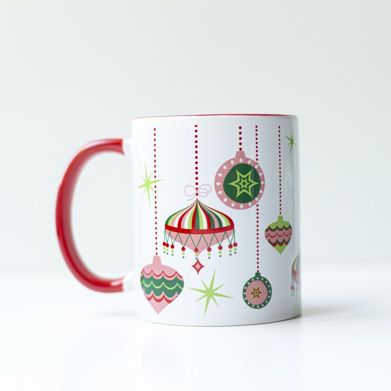 Pink, green, red, and white 1950s style retro ornaments at different hanging heights from the top edge of the mug on a white background. Inside of the mug is red, and the handle is red