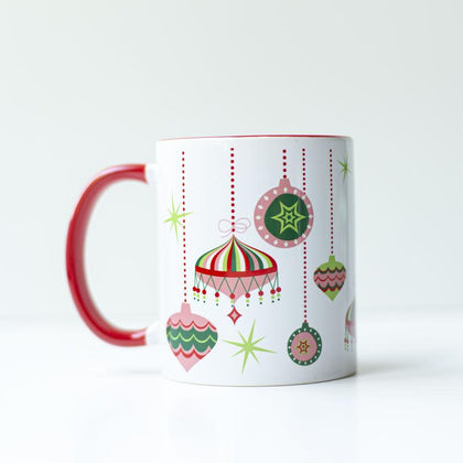 Pink, green, red, and white 1950s style retro ornaments at different hanging heights from the top edge of the mug on a white background. Inside of the mug is red, and the handle is red