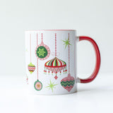 Pink, green, red, and white 1950s style retro ornaments at different hanging heights from the top edge of the mug on a white background. Inside of the mug is red, and the handle is red