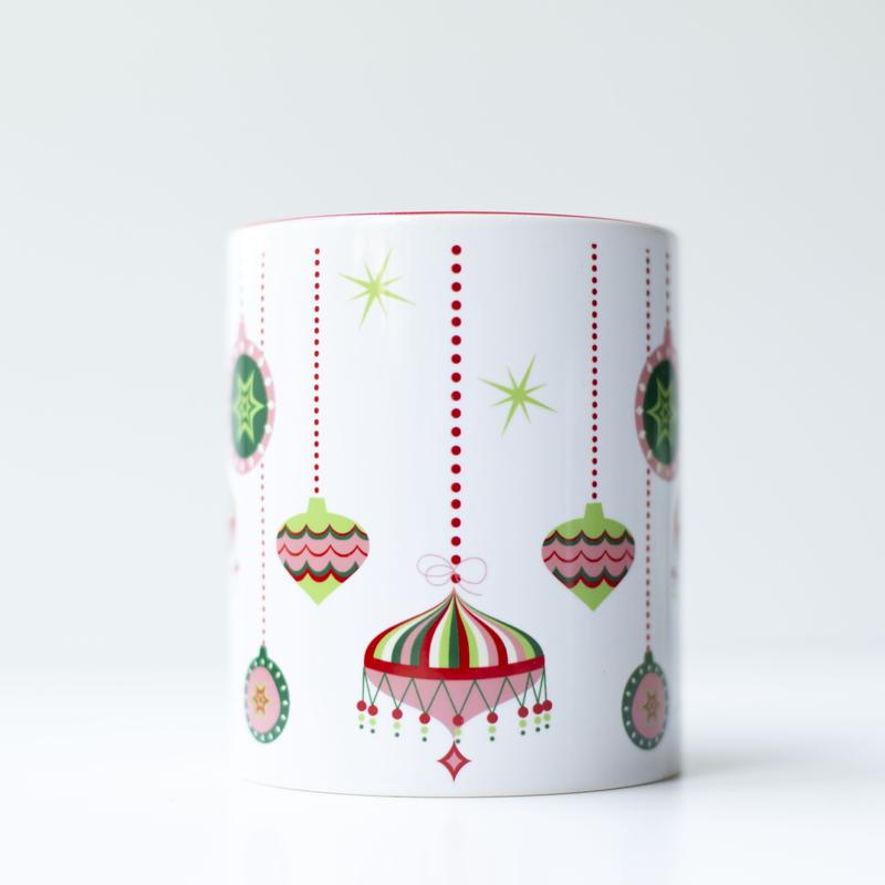 Pink, green, red, and white 1950s style retro ornaments at different hanging heights from the top edge of the mug on a white background. Inside of the mug is red, and the handle is red