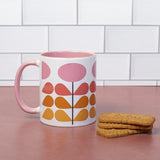 1959s mid century modern pink flowers on a white background coffee mug. Has ombre orange to yellow leaves. Inside of mug is pink, and the handle is also pink. This photo shows the mug next to brown rectangle cookies