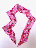 This photo shows the hair scarf unfolded. Scarf is like pink with various pink cherries decorating it.