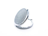 A round compact mirror with silver holographic glitter on one side of it. Compact has a small button to open the mirror. Photo shows mirror open with showing the glitter side of mirror