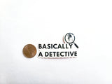 The phrase "basically a detective" with a magnifying glass that has a zoomed in picture of a fingerprint. Sticker is next to a quarter to show size