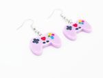 Light purple Video game controller earrings that are styled like xbox controllers as earrings. Has a red painted heart in the middled of the controller. Photo shows earrings fro a side angle