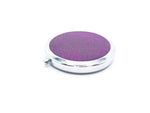 A round compact with Purple glitter on one side of it. Compact has a small button to open the mirror