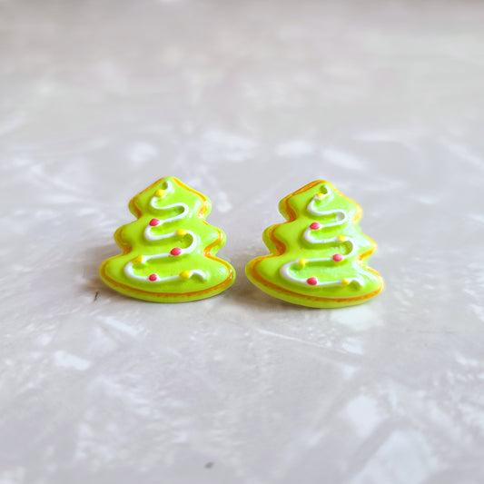 Photo shows the earrings up close. Earrings are pine tree shaped with light green frosting background and a white frosting line in a zig zag with yellow and red dots to look like ornaments