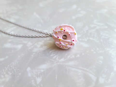 This photo shows a zoomed in look at the donut clip. The donue is a pink donue with white zig zag frosting that includes red and yellow sprinkles