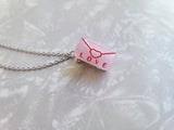 This photo shows a close up of the swearer clip. It is a small, light pink envelope with red details. Also has red lettering of the word "love"