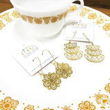 This photo shows the Pyrex Flower earrings and the Stacked Bowl Earrings on a white Pyrex Plate that has the Flower pattern in gold. There is also a Pyrex cup with the same pattern sitting on the plate as well