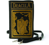 Black vinyl rectangle shaped purse with gold detailing of Dracula with a victim in a cave like setting. Cave features a skull, wall sconce, a bat, and a spider. DRACULA in big bold gold letters across the top
