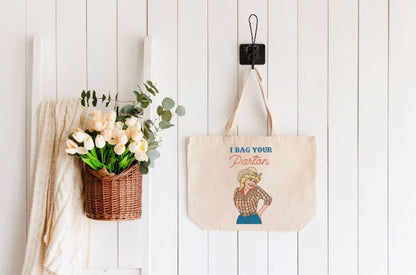 Photo shows the bag being displayed on a white wall with a plant to the left. Bag has Dolly Parton and the phrase "I bag your Parton" on it