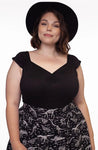 This photo shows a female presenting model wearing the top in a close up of the top. Model has short brown hair and is wearing a black hat.