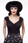 This photo shows a female presenting model wearing the top. Top is black. Model has black hair with bangs, and is wearing a black hat
