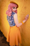 This photo shows a female presenting model wearing the skirt. Skirt is above the knee, and has an elastic section in the back. Model has pink hair and is wearing a yellow beret