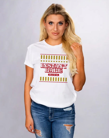 This photo showcases a female presenting White model with blonde hair wearing the Instant Babe T shirt. Shirt is white and is made to look like an Instant Noodle cup but replacing the wording to Instant Babe