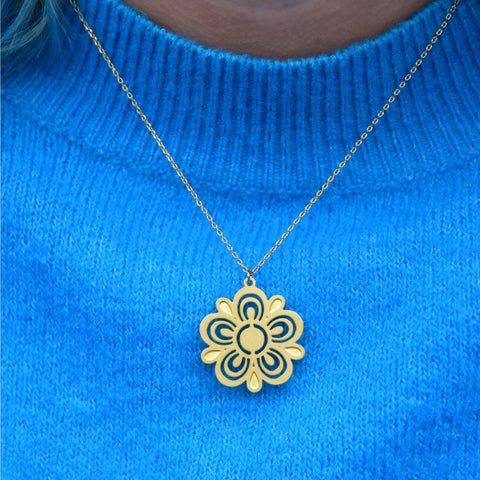 This photo shows an up close look at the Pyrex Flower Necklace. Necklace is gold, and is shown against a blue sweater