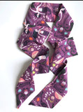 This photo shows the hair scarf unwound to showcase the length of it. This scarf has different mermaids with dark colored tails, pink whales, and various sea plants on a dark purple background