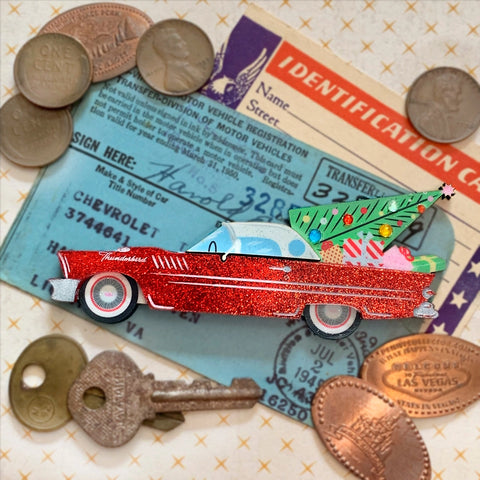 This photo shows the brooch against an old drivers license, and surrounded by wheat pennies. Brooch is a red thunderbird with a retro style Christmas tree, and presents in the back