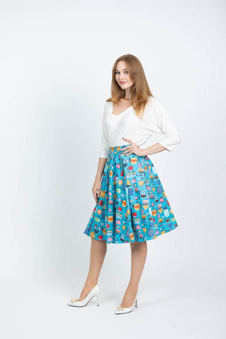 This photo shows a white female presenting model wearing a white blouse with the Kitchenware skirt. Skirt has a array of vintage kitchen items such as mixing bowls, tea kettles, mugs, etc on a light blue background.  Model is shown with her hand on her hip