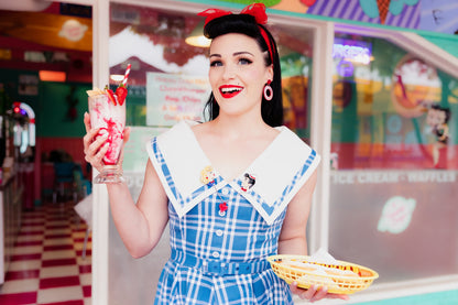 Female model wearing brooch while holding a milkshake and a hot dog